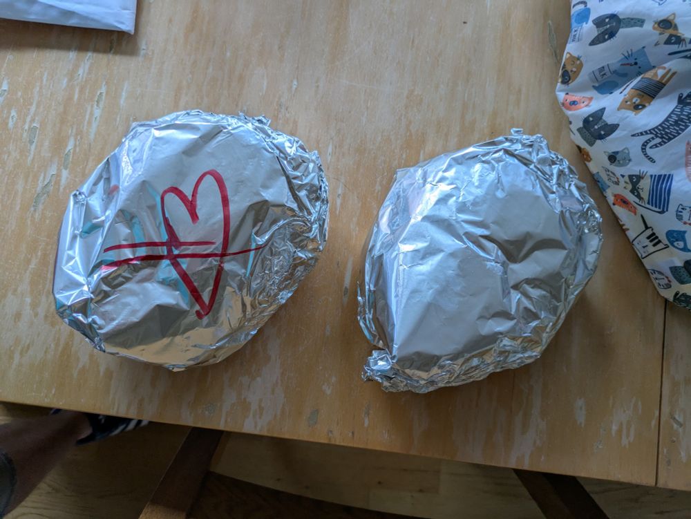 Zwei in Alufolie eingepackte Döner auf einem Holztisch. Auf einem ist ein rotes Herz aufgemalt.