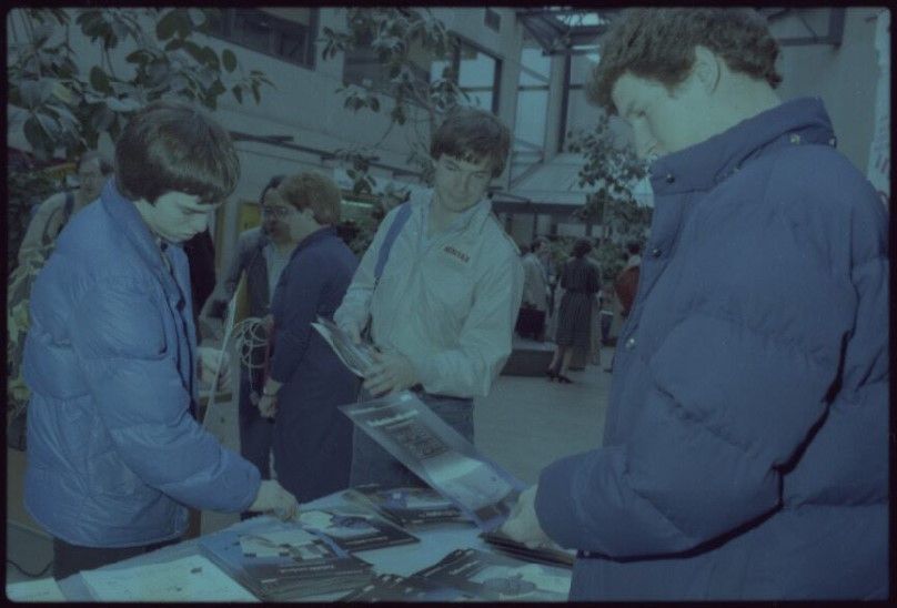 Young people, presumably college students, peruse written materials from Digital Equipment Corp's display on campus at Rochester Institute of Technology in 1983.