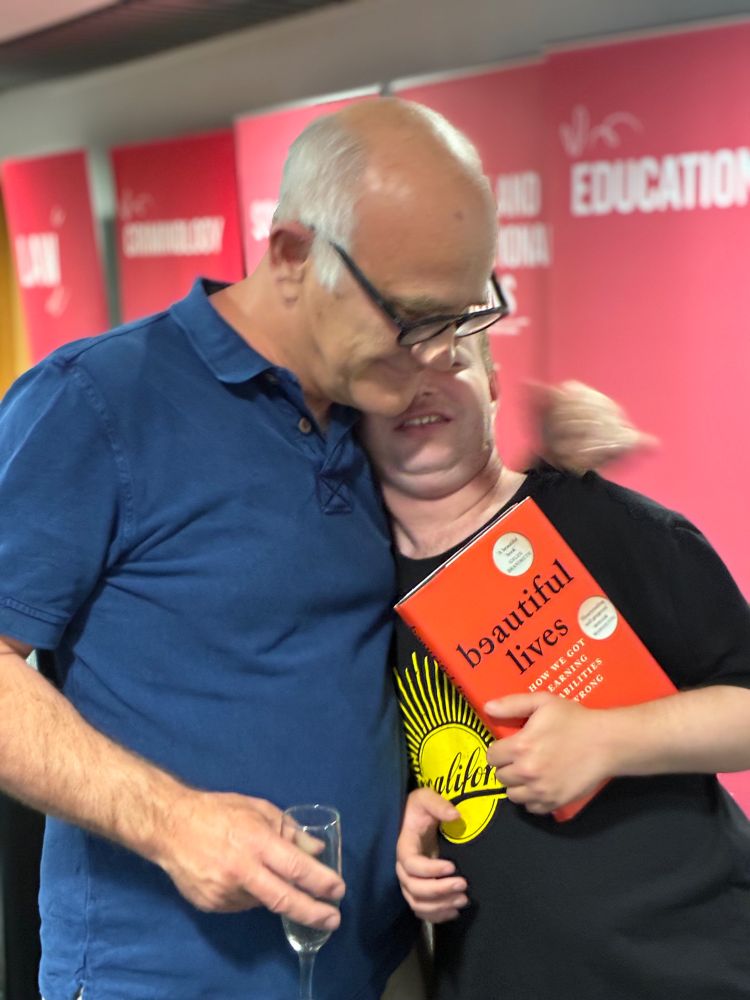 Stephen and his son Joey hug while Joey holds a copy of Beautiful Lives in his hand and leans into his dad.