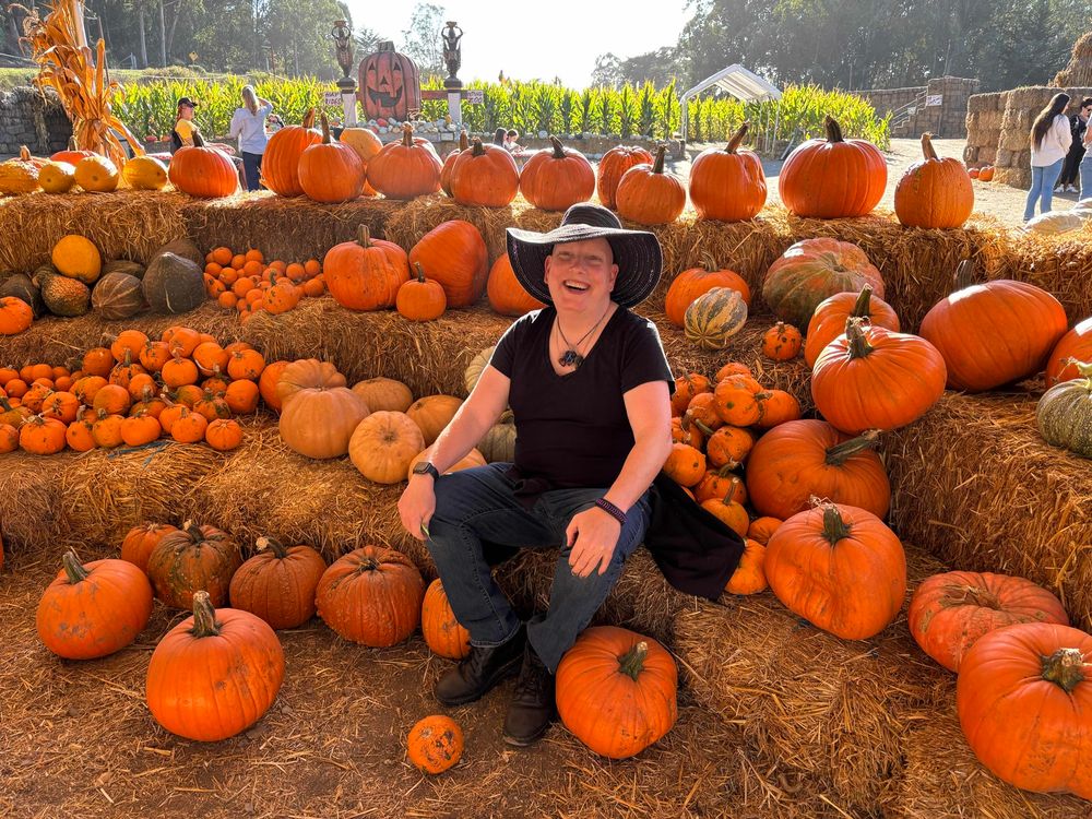 Me smiling and sitting on hay bales and surrounded by pumpkins 