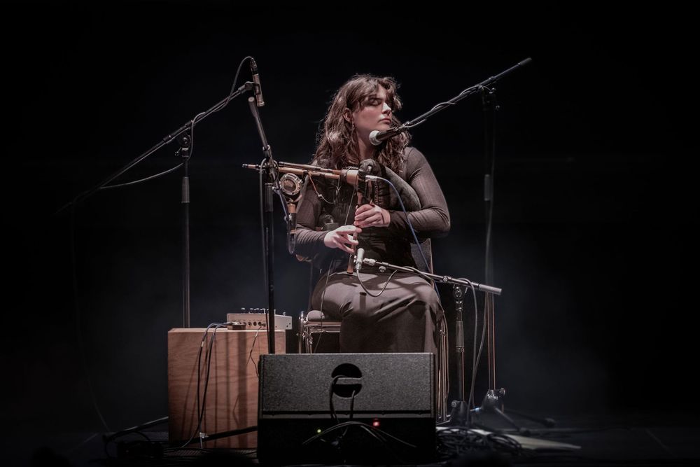 Photo of Brìghde Chaimbeul playing pipes on stage, surrounded by microphones. 
