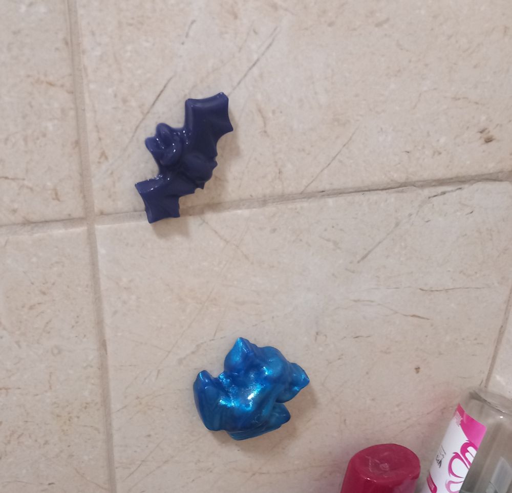 A shiny blue frog and a dark purple bat stuck on some tile in a bathroom. 