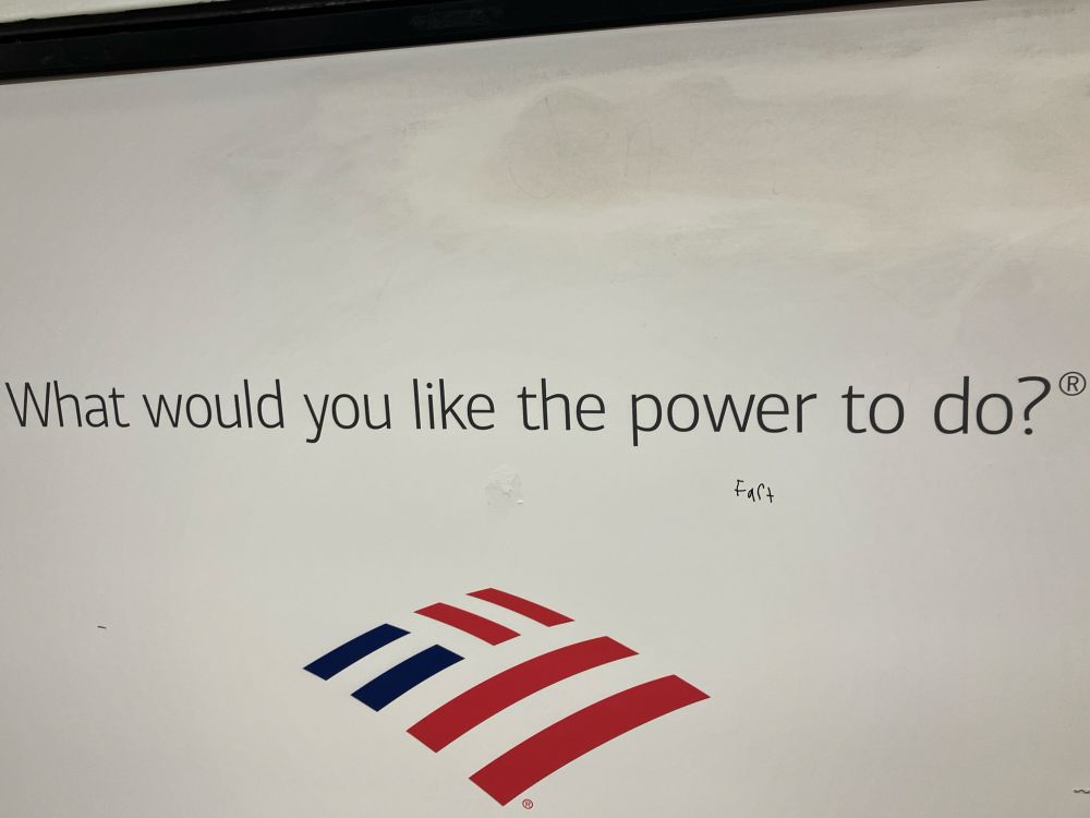 Mostly empty advertisement for a bank with text “What would you like the power to do?” below in small uneven letters someone has graffitied “fart” 