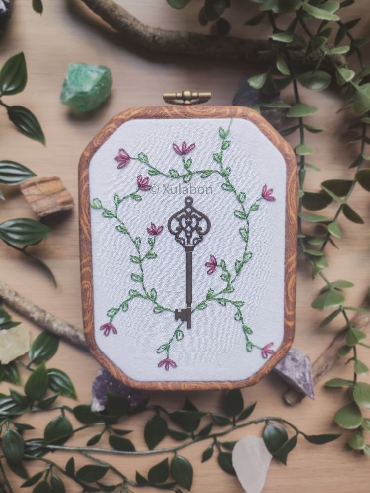 Broderie avec une clef attachée au centre et des lianes de fleurs roses brodées autour 