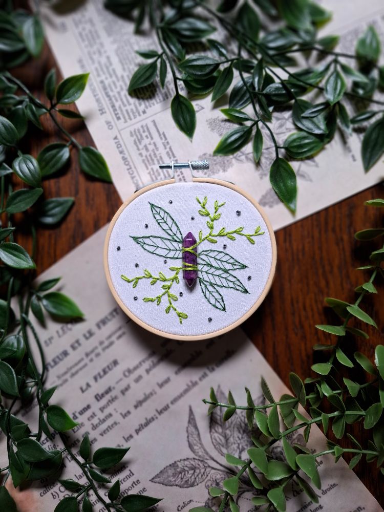Broderie d'une pierre violette avec des plantes brodées autour