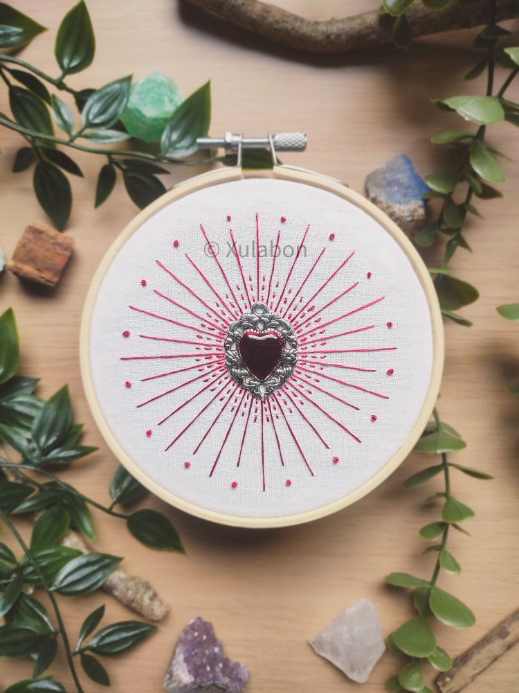 Cœur rouge en métal attaché au centre avec des traits circulaires autour de ce cœur brodé avec du fil rouge satin