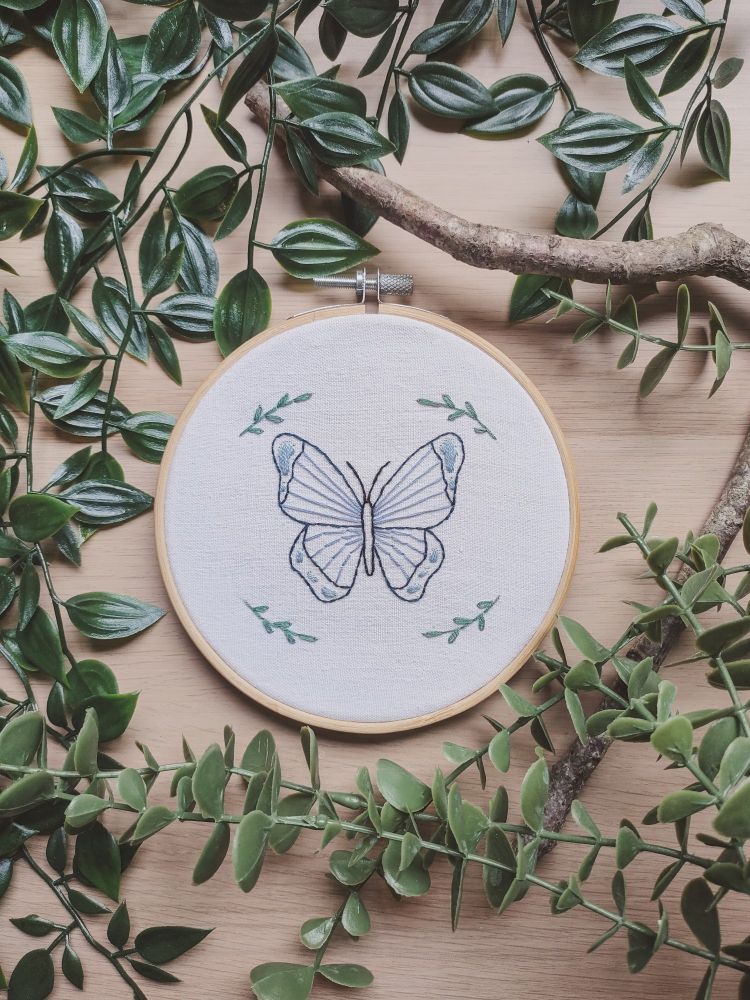 Broderie d'un papillon bleu avec des petites feuilles brodées dans les 4 coins autour 