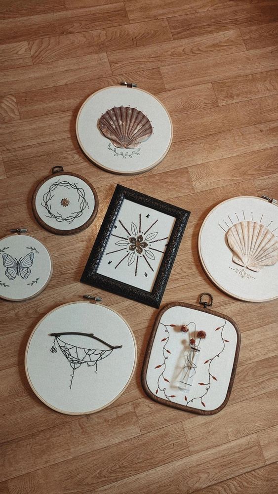 Photo de groupe de mes broderies avec 2 broderies coquillage en haut (une plus à droite). Ensuite on a la broderie breloque de fleur en couronne de liane, la broderie breloque de fleur en cadre avec ornement brodés. Ensuite en bas de gauche à droite on a la broderie papillon bleu avec des petites branches de feuilles, la broderie toile d'araignée avec une vraie branche et la broderie vase avec lianes de feuilles d'automne.