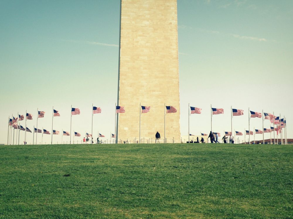 looking up the hillside at the base of the washington monument where you can see some tourists and most of the ring of flagpoles