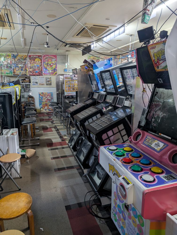 Arcade cabinets lined up in a narrow walkway in a hall. There's old pop n music, jubeat and more