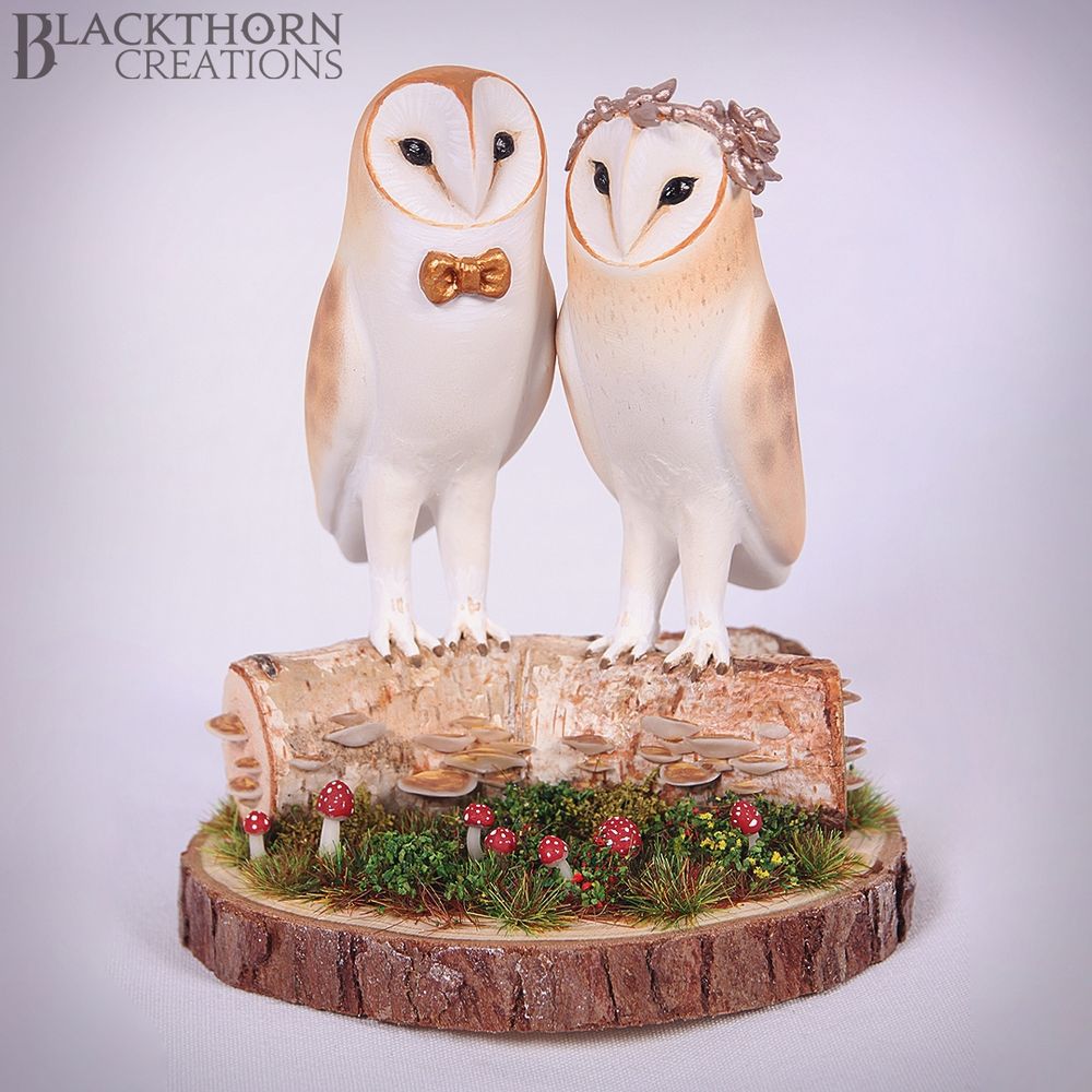 Two Barn owls standing on a log with fungi growing out of it. One Barn Owl has a bowtie on and the other a rose gold flower crown. 