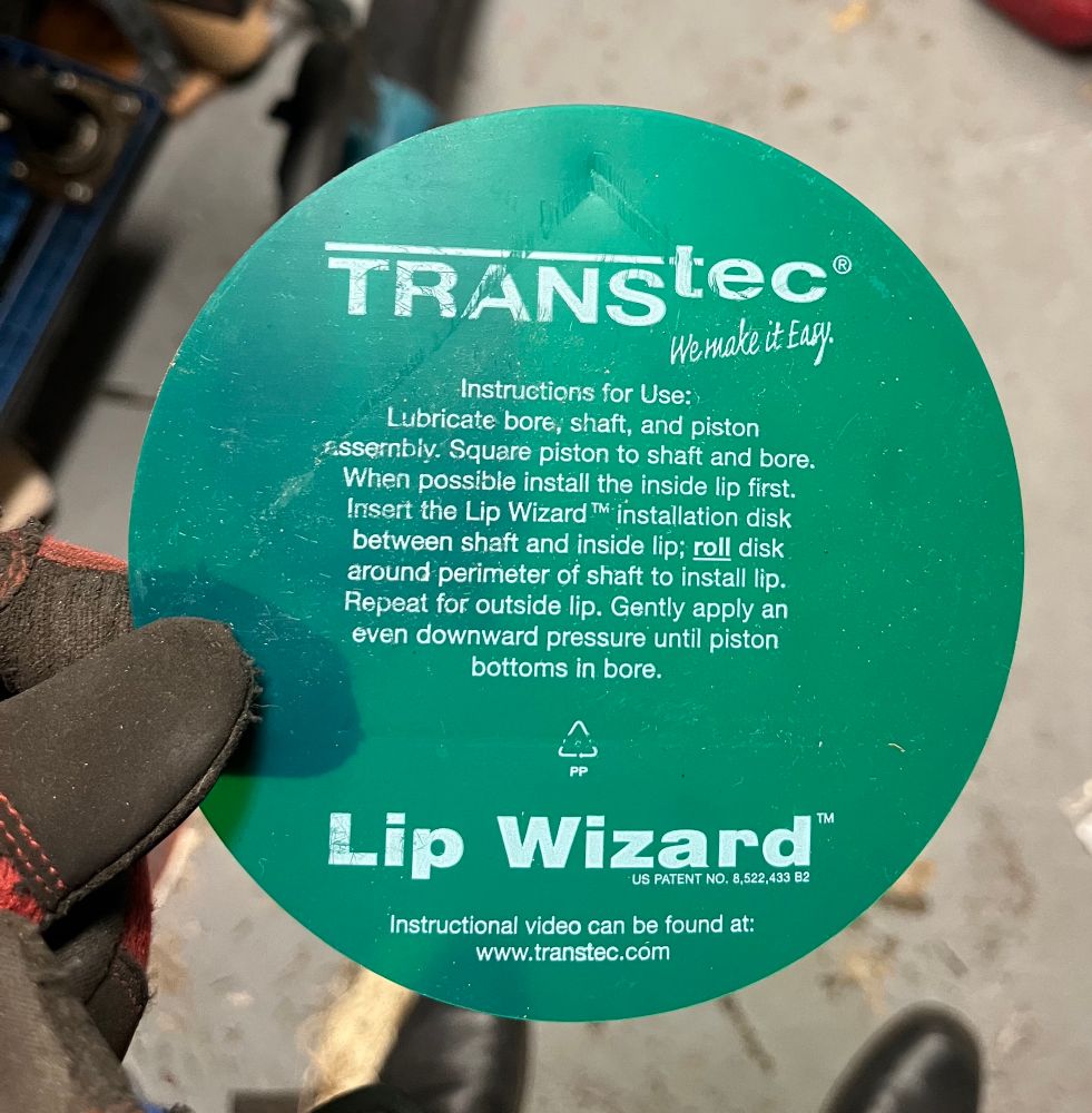 A green label that says

TRANSteC®
We make it Easy.
Instructions for Use:
Lubricate bore, shaft, and piston
assembly. Square piston to shaft and bore.
When possible install the inside lip first.
Insert the Lip Wizard ™ installation disk between shaft and inside lip; roll disk around perimeter of shaft to install lip.
Repeat for outside lip. Gently apply an even downward pressure until piston bottoms in bore.
Lip Wizard™
