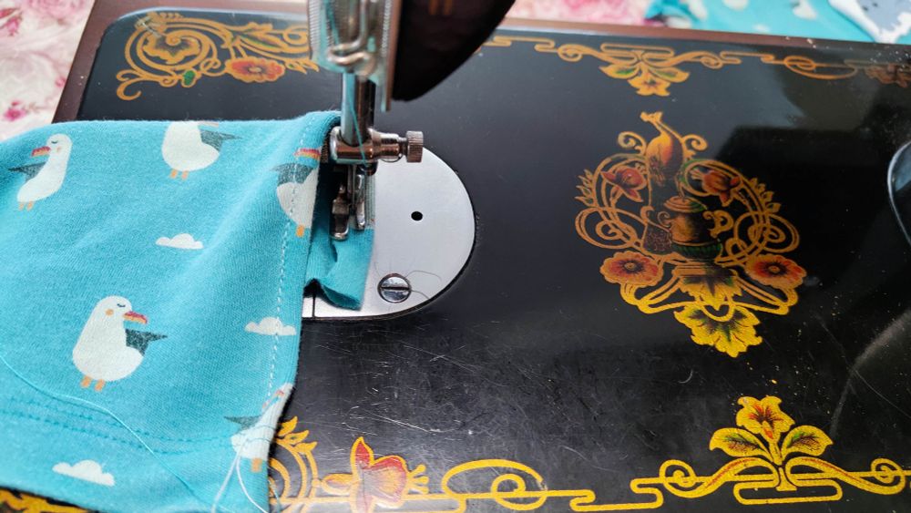 Sewing a teal blouse with seagulls on an old Union sewing machine with a painted peacock 