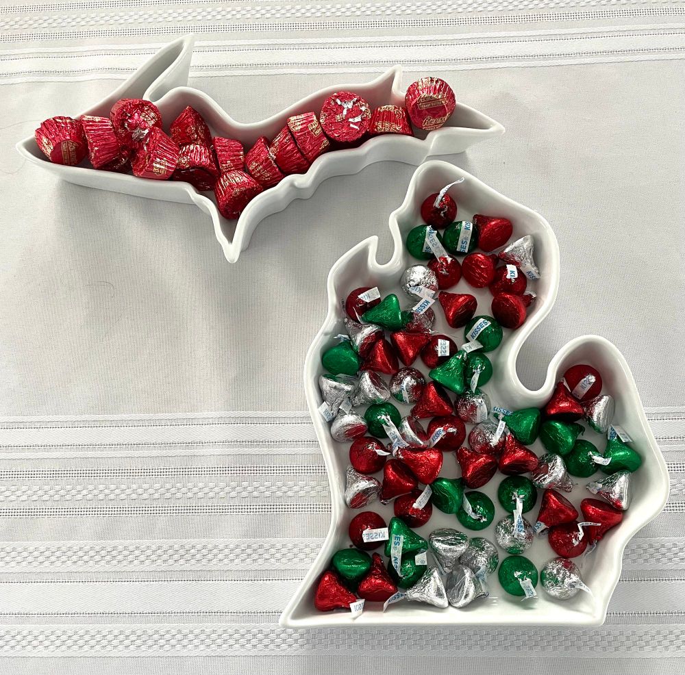 Two white porcelain serving dishes in the shape of the upper and lower peninsulas of Michigan. Red-wrapped Reese’s peanut butter cups are in the upper dish, and red, green and silver Hershey Kisses are in the lower dish.