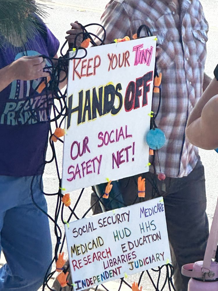 Keep your hands off our social safety net sign w list of many pieces of what that means— social security, Medicare, Medicaid, hud, hhs, research, education, libraries, independent judiciary