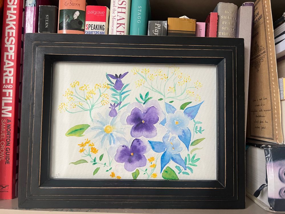 A framed floral watercolor sitting on a shelf of books about Shakespeare. The watercolor flowers are pansies, columbine, fennel, daisies, rue, and rosemary. 