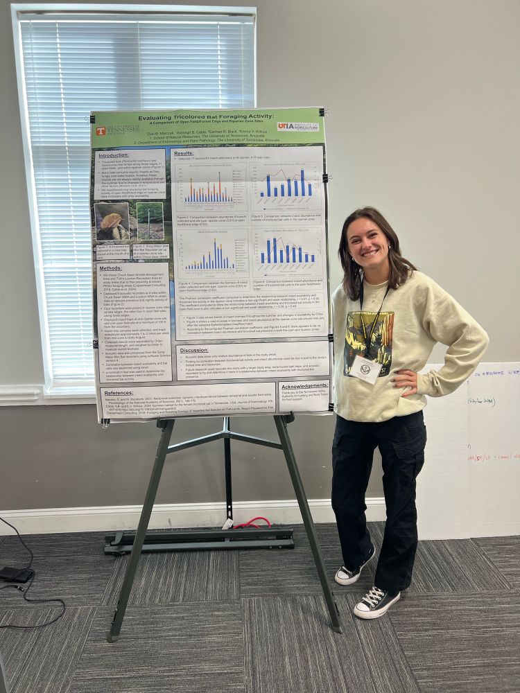 A researcher stands with a research poster
