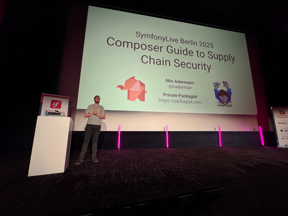 Nils Adermann standing on a stage next to a podium and in front of a large screen saying "Composer Guide to Supply Chain Security" with a Packagist elephant logo and a Composer logo
