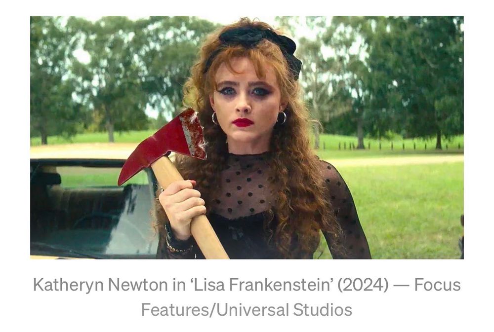 Katheryn Newton as Lisa in Lisa Frankenstein (2024) in a dramatic black dress holding a bloody ax in a green graveyard in daylight.