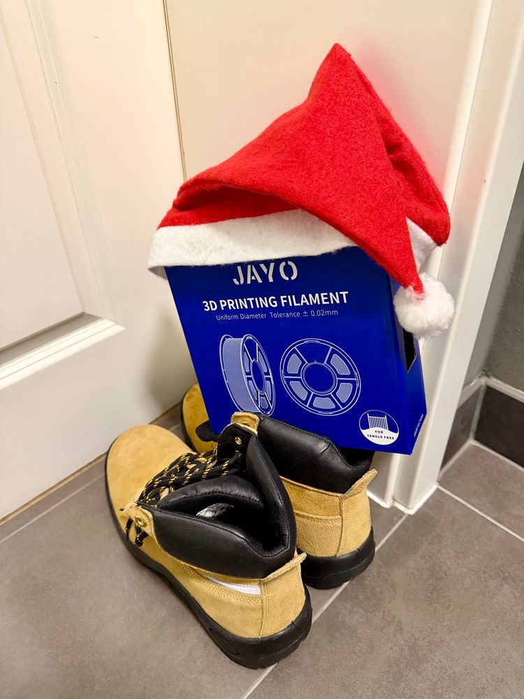 Zwei helle Stiefel mit einem blauen Karton JAYO-Filament.

Der Karton hat eine rote Weihnachtsmann-Mütze auf. 