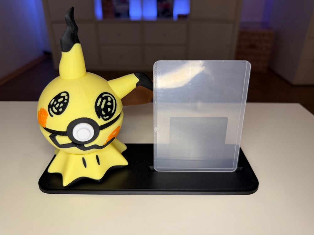 Links ein Pokéball, der wie Mimigma aussieht.
Rechts ein leerer Top-Loader.