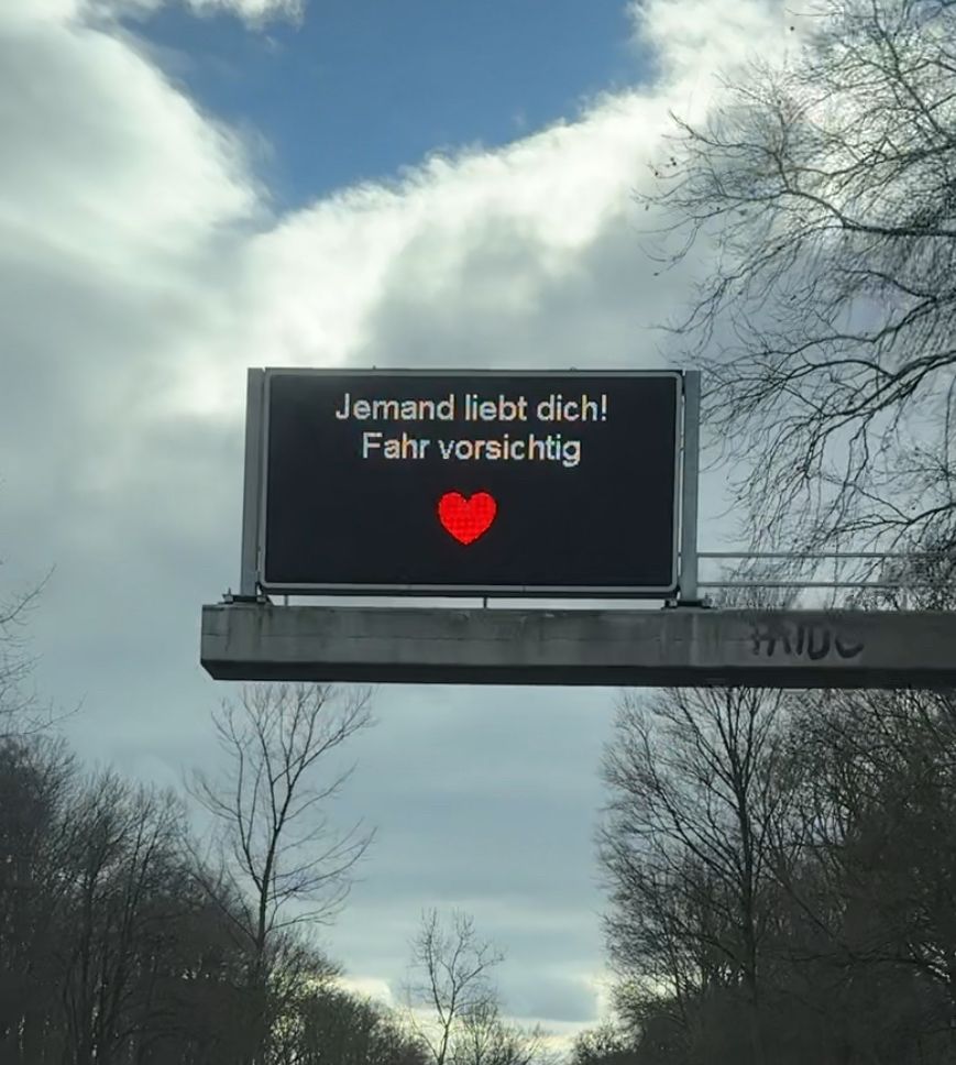 Verkehrstafel, auf der "Jemand liebt dich! Fahr vorsichtig ♥️" steht. 