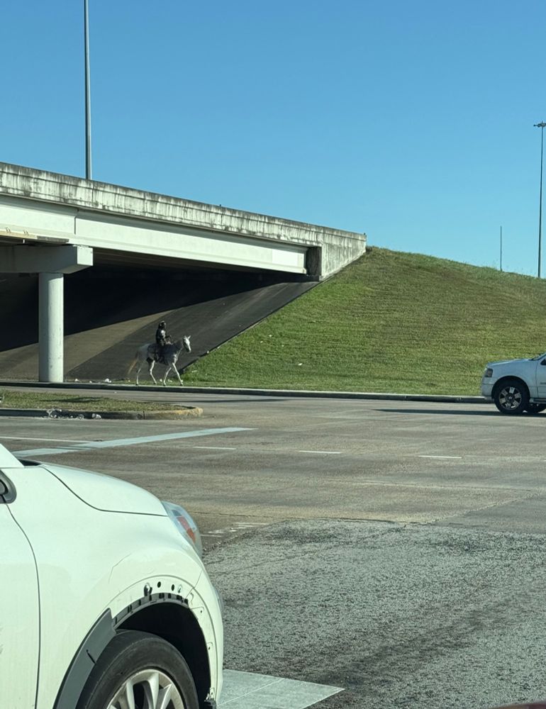A Black man wearing big headphones on a horse going under a freeway overpass. 