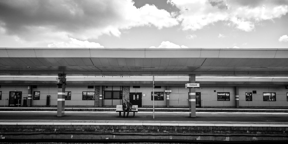 Black and white image of a solitary man sitting on an empty train station in Oxford, UK