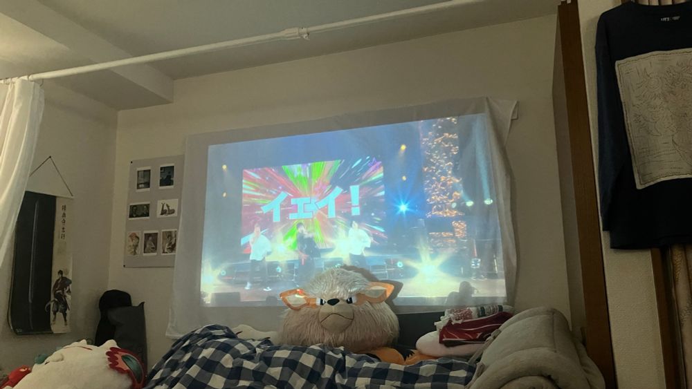 部屋　ベッドの奥の壁にプロジェクター投影中WITHのライブ円盤、場面はアサヒのソロ曲で「イェイ！」と大きく表示されている

投影画面の手前にウインディのぬいぐるみで少し投影の邪魔になっている