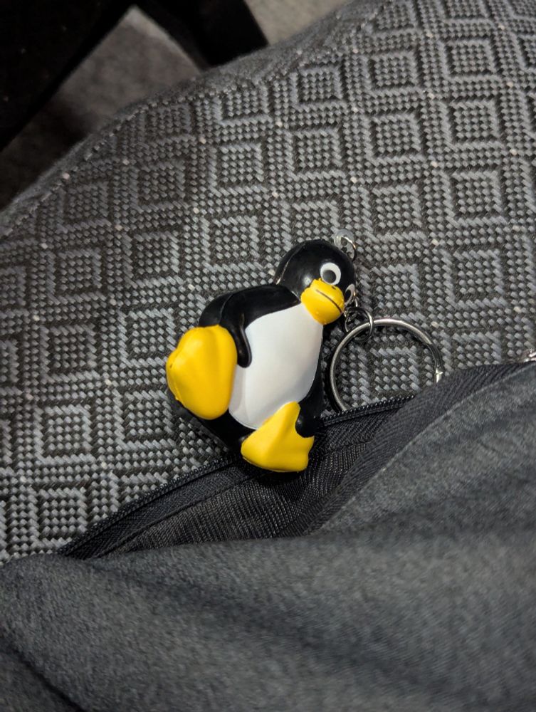 Penguin (Tux) squishy keychain just out of my pocket on a chair
