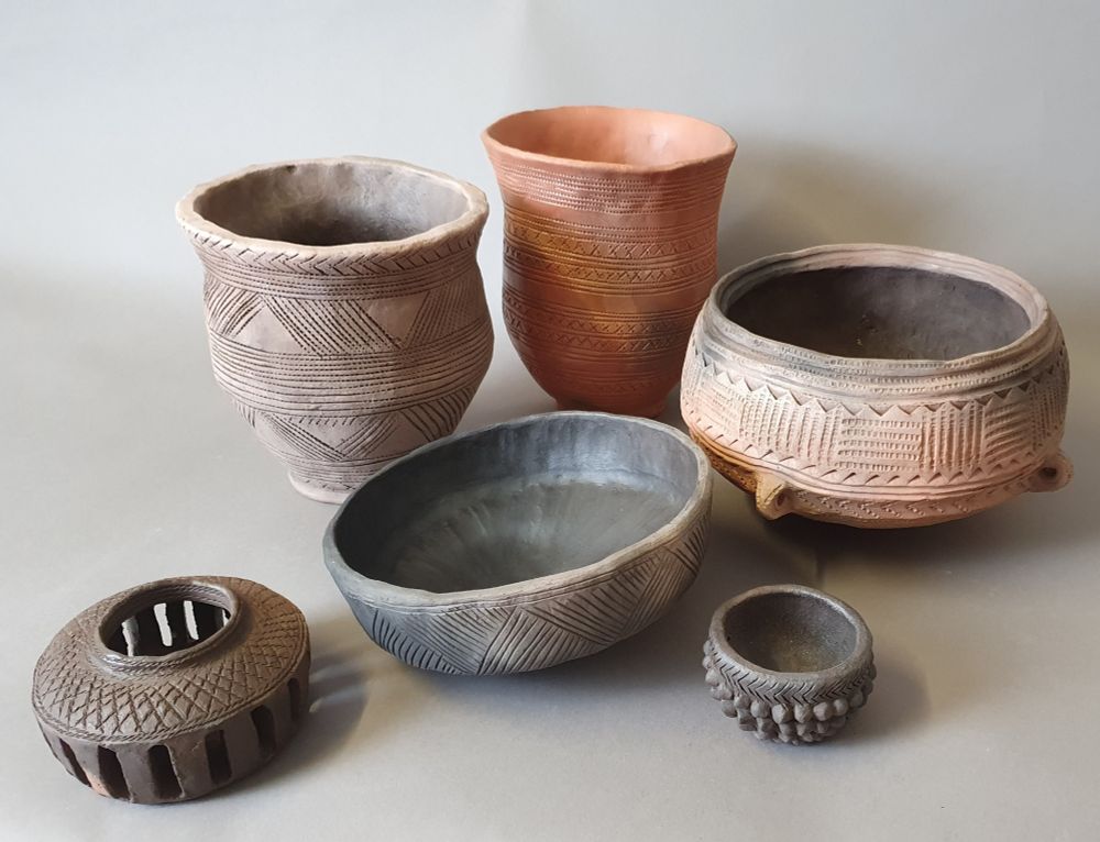 A group of replica British prehistoric pots by Potted History. Hand formed and coloured from red through buff and grey to black, and showing the variations in colour that result from being fired in an open fire.