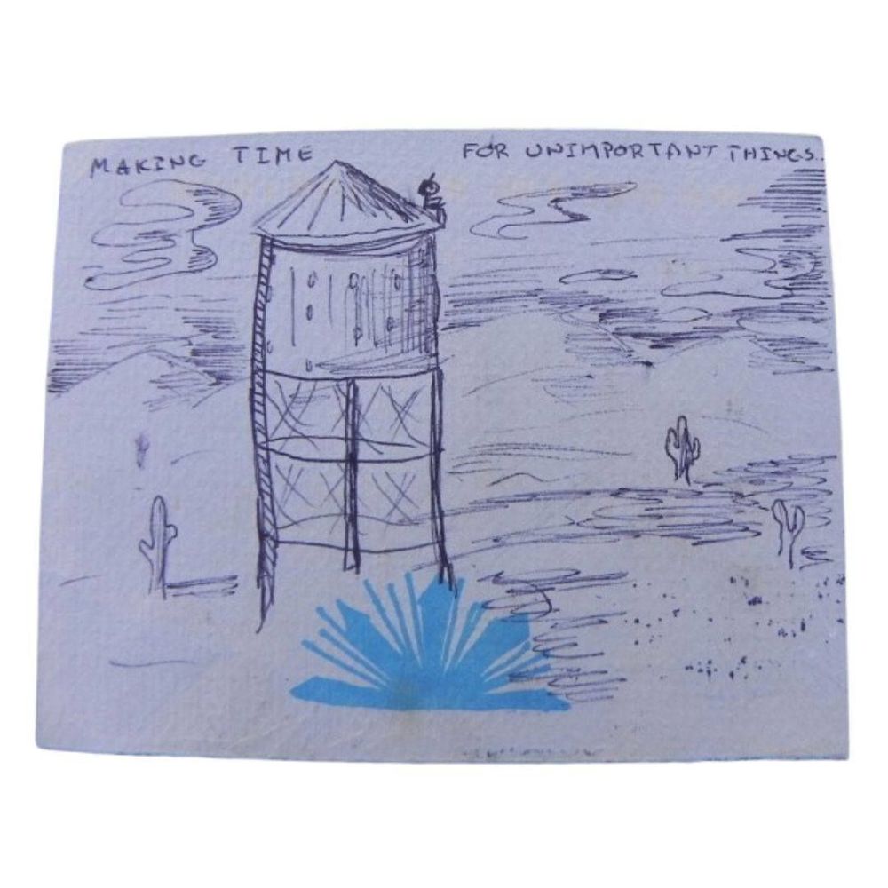 A postcard with a pen drawing of a desert over a blue crystal print. There's a water tower, some cacti, some hills. A little stick figure sits on top of the tower, and the words say "Making time for unimportant things".