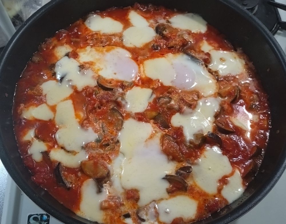 フライパンいっぱいのトマトの煮込みの上に、とけたモッツァレラチーズが散らばっている