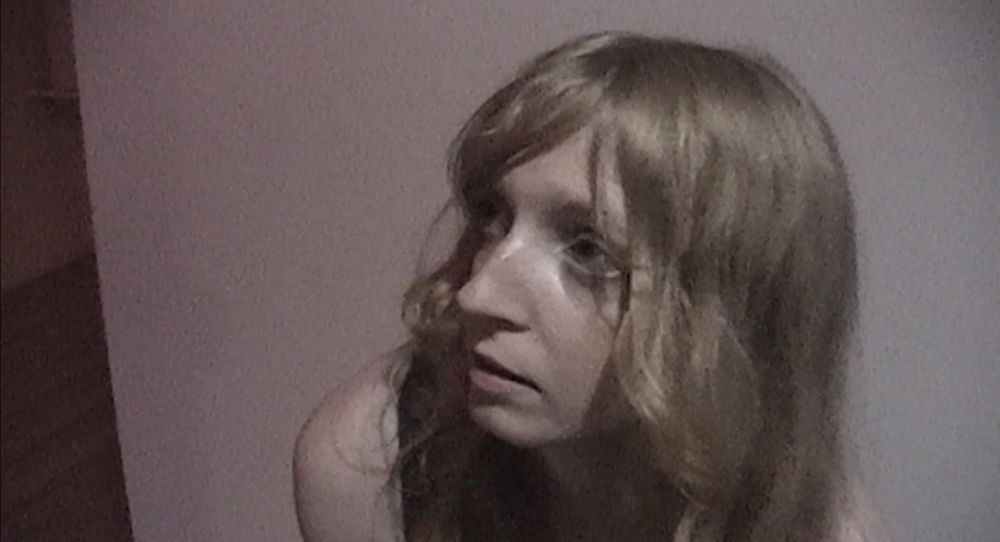 lex walton looks up with her big eyes, sitting against a white wall