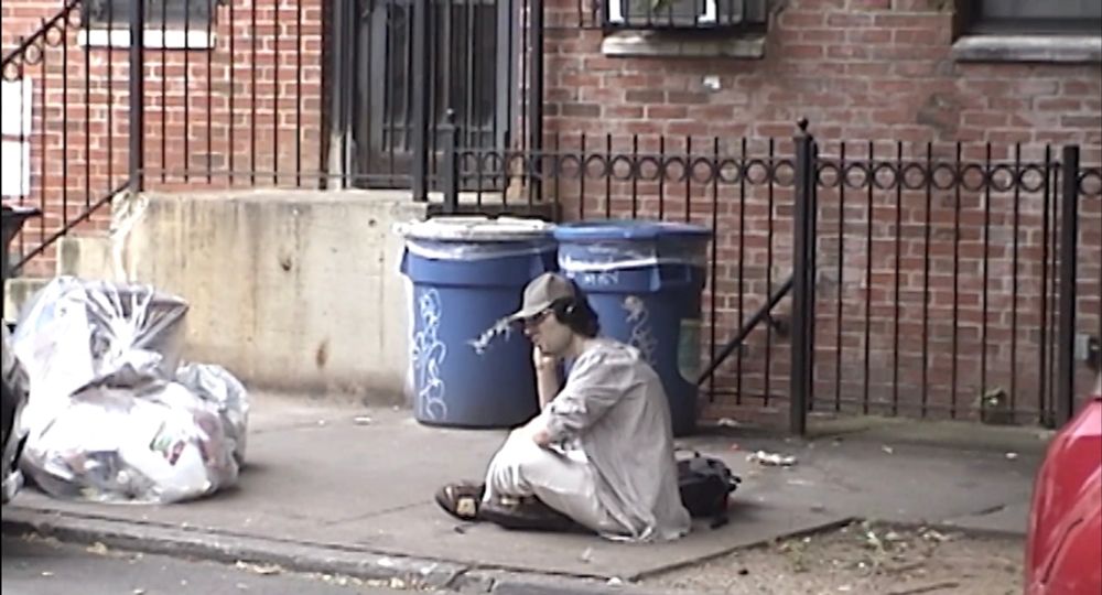 a man sits on the street, listening to headphones