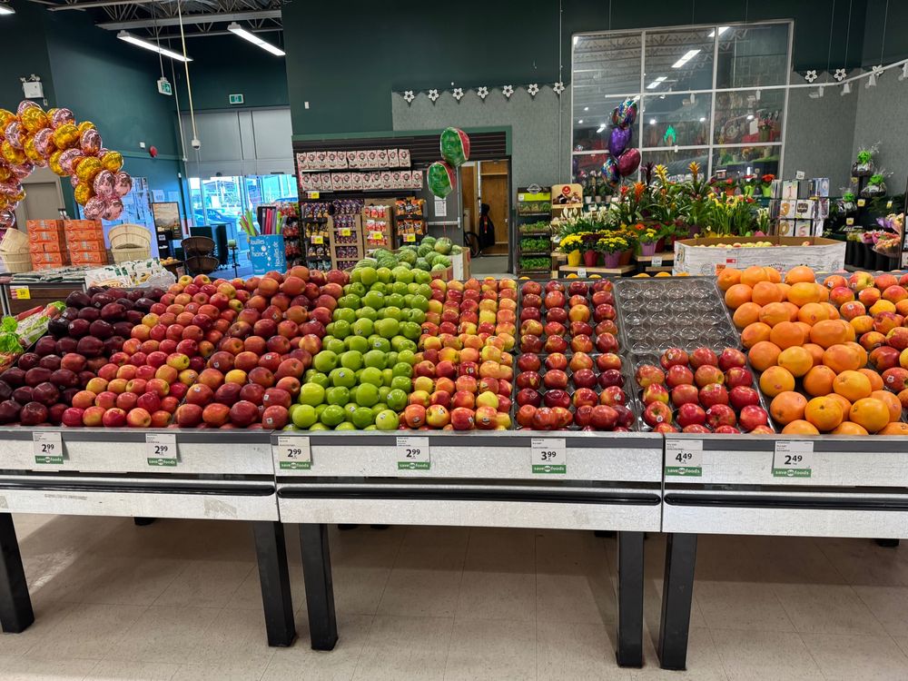 A supermarket display of a 7 varieties of apples, and some oranges. All sections full except 1. 
