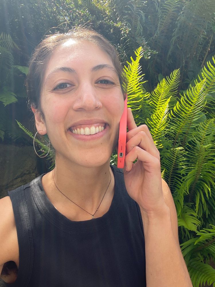 A woman with brown hair smiling big on the phone