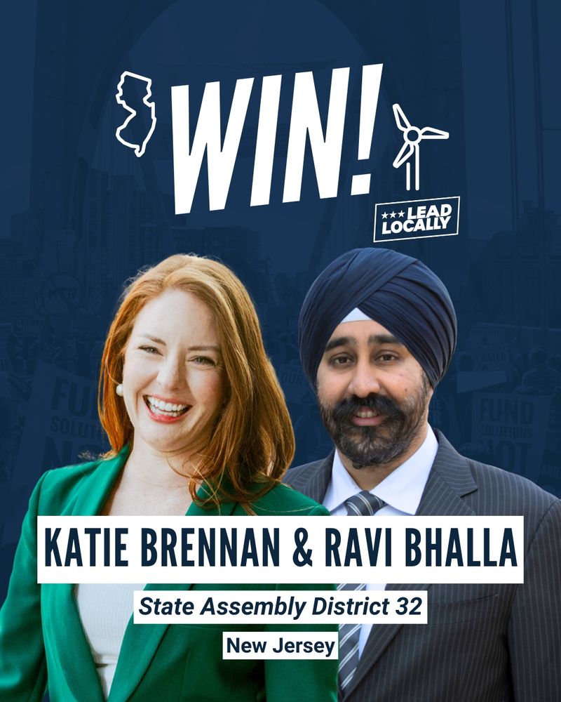 Two people smiling. The woman on the right has red hair and is wearing a green jacket. The man on the right is wearing a head wrap and a gray suit jacket.