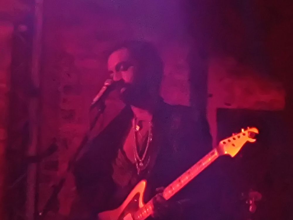 Guitarist in Mandrake Handshake. Purple light shines on him as he grooves with eyes closed