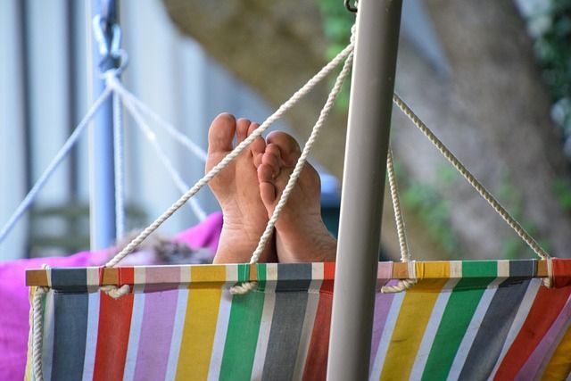 Das Foto zeigt eine Hängematte mit bunten Längsstreifen von der Schmalseite her fotografiert. Über die Unterkante der Hängematte schaut ein Paar nackter Füße.
