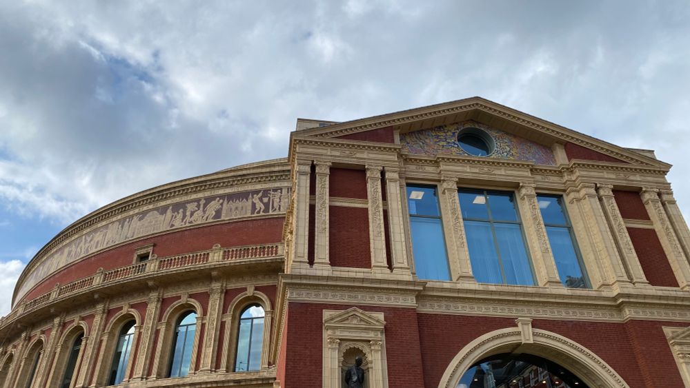 Looking at Door 12 of the Royal Albert Hall: a brick built building with stone mouldings around doors and windows and a frieze of terracotta tiles around the top