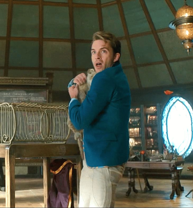 Jonathan Bailey in a still from the movie wicked. He is attempting to hide a lion cub in his jacket.