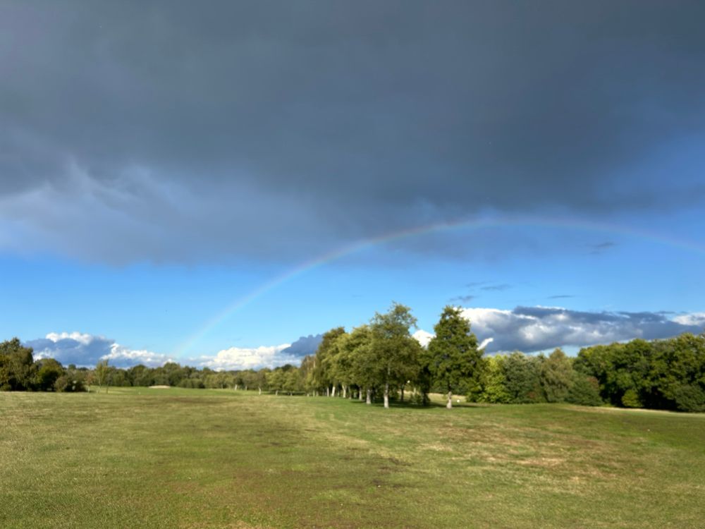 A golf course with some blue skies, some dark cloud and a rainbow 