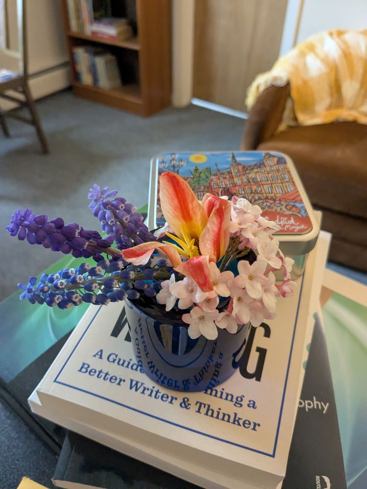 A tiny bud vase with a few flowers sits atop a stack of books in an office. 