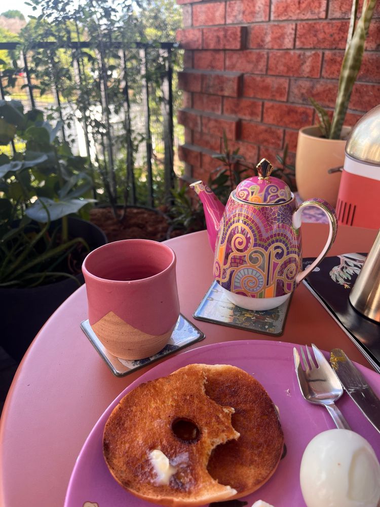Bagel and egg on a pink plant with a pink teapot and cup. All out on a leafy balcony. Always a splayd! 