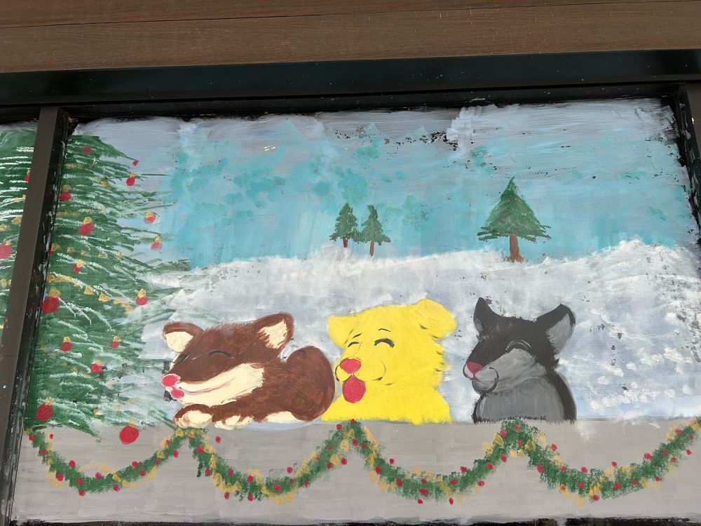 Window painting of Christmas trees, garland, and 3 puppies.