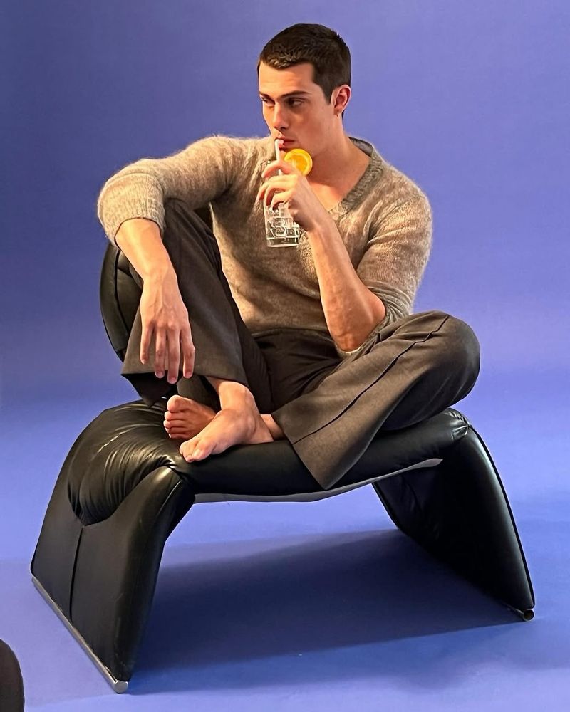 As shared on IG, barefoot Nick Galitzine sits on a delightful leather bench finishing his drink and looking off camera.  
