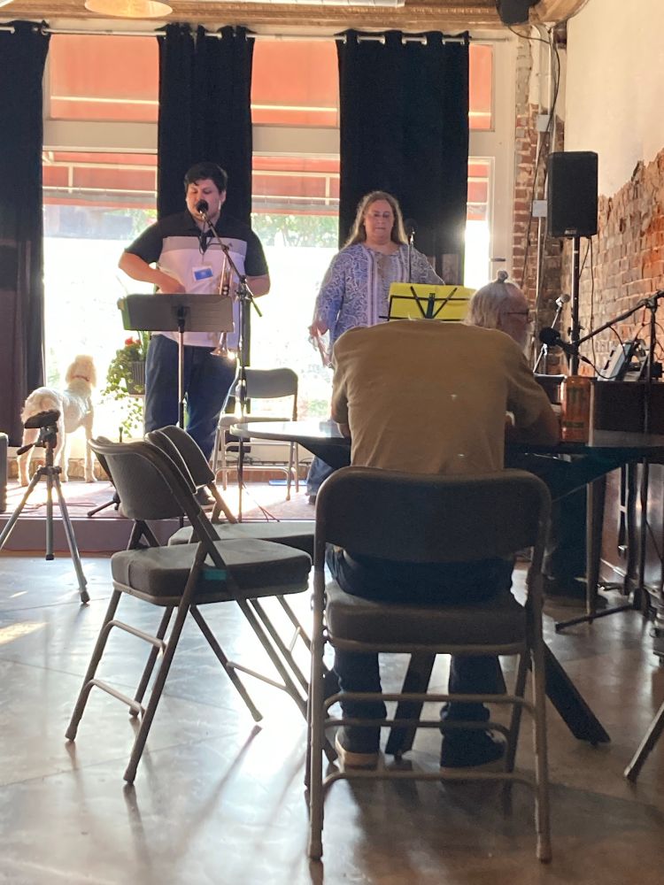 The roadie for the jazz trio was having a hard day. (Man with head on table listening to a jazz combo.)