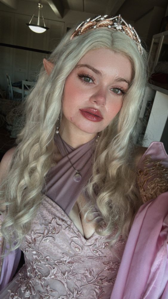 Selfie of the same woman in a silver wig and light mauve gown, as well as elf ears
