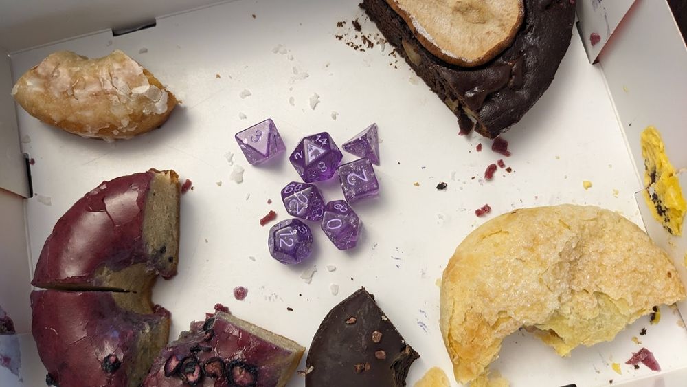 a full set of sparkly purple dice in the middle of a box of half eaten doughnuts